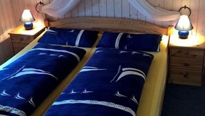 Ein Schlafzimmer einer Holzhütte mit einem mit blauem Bettzeug bezogenen Bett, zwei Nachttischlampen und einem Himmelbett.