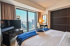 Ein Hotelzimmer mit einem großen Bett, einem Fernseher, einem Schreibtisch mit Lampe und Blick auf die Stadt.