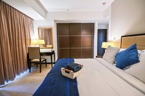 Ein Hotelzimmer mit einem Bett, einem Schreibtisch, einem Stuhl und einem großen Fenster mit Vorhängen.