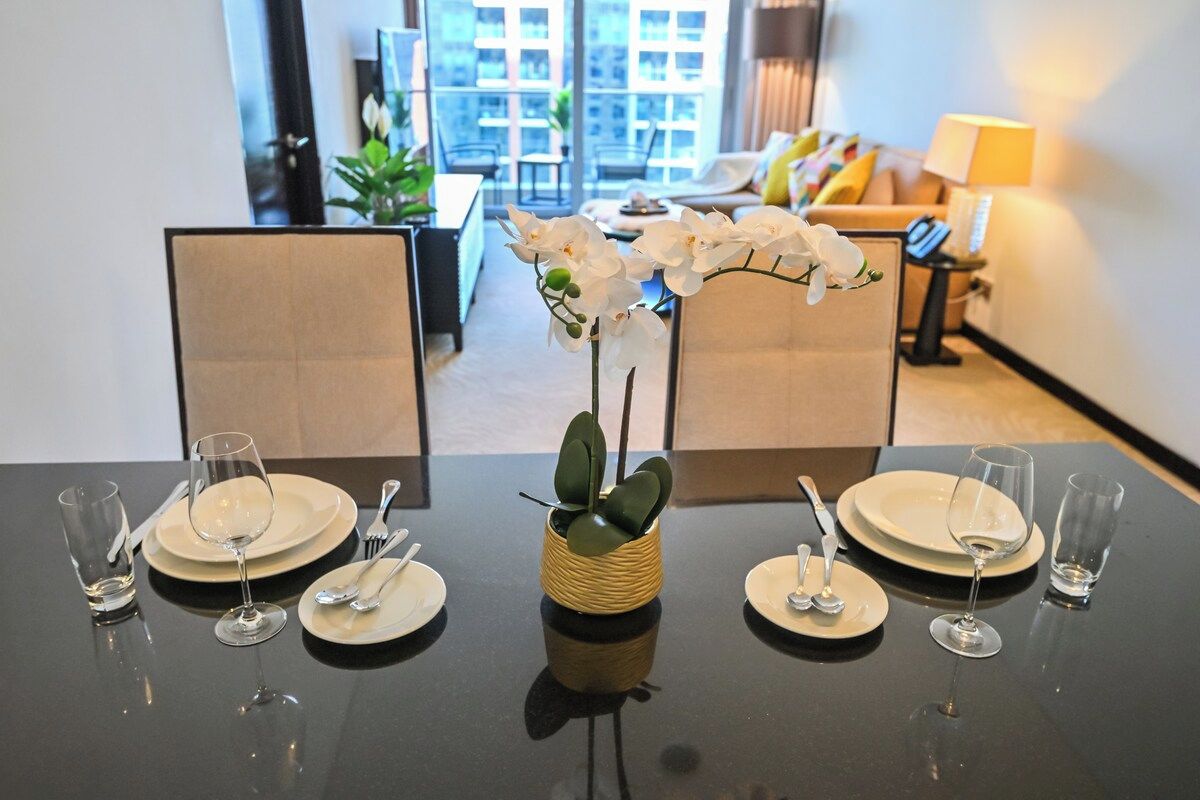 A dining table set with plates, cutlery, and a vase with white flowers.