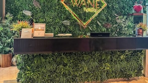 A reception desk with a neon sign that reads 'WANE' surrounded by a lush green wall. - Luxury Marina 1-Bedroom - 5-star Hotel Amenities (Dubai)