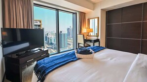 A hotel room with a large bed, a TV, a desk with a lamp, and a view of the city through large windows. - Luxury Marina 1-Bedroom - 5-star Hotel Amenities (Dubai)