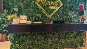 Un comptoir d'accueil avec un panneau néon sur lequel on peut lire « WANE » et un décor de feuillage verdoyant en arrière-plan.