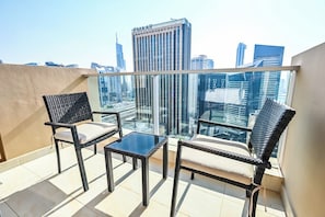 Un balcon avec deux fauteuils en osier et une petite table, d’où l’on peut admirer un paysage urbain avec des bâtiments modernes.