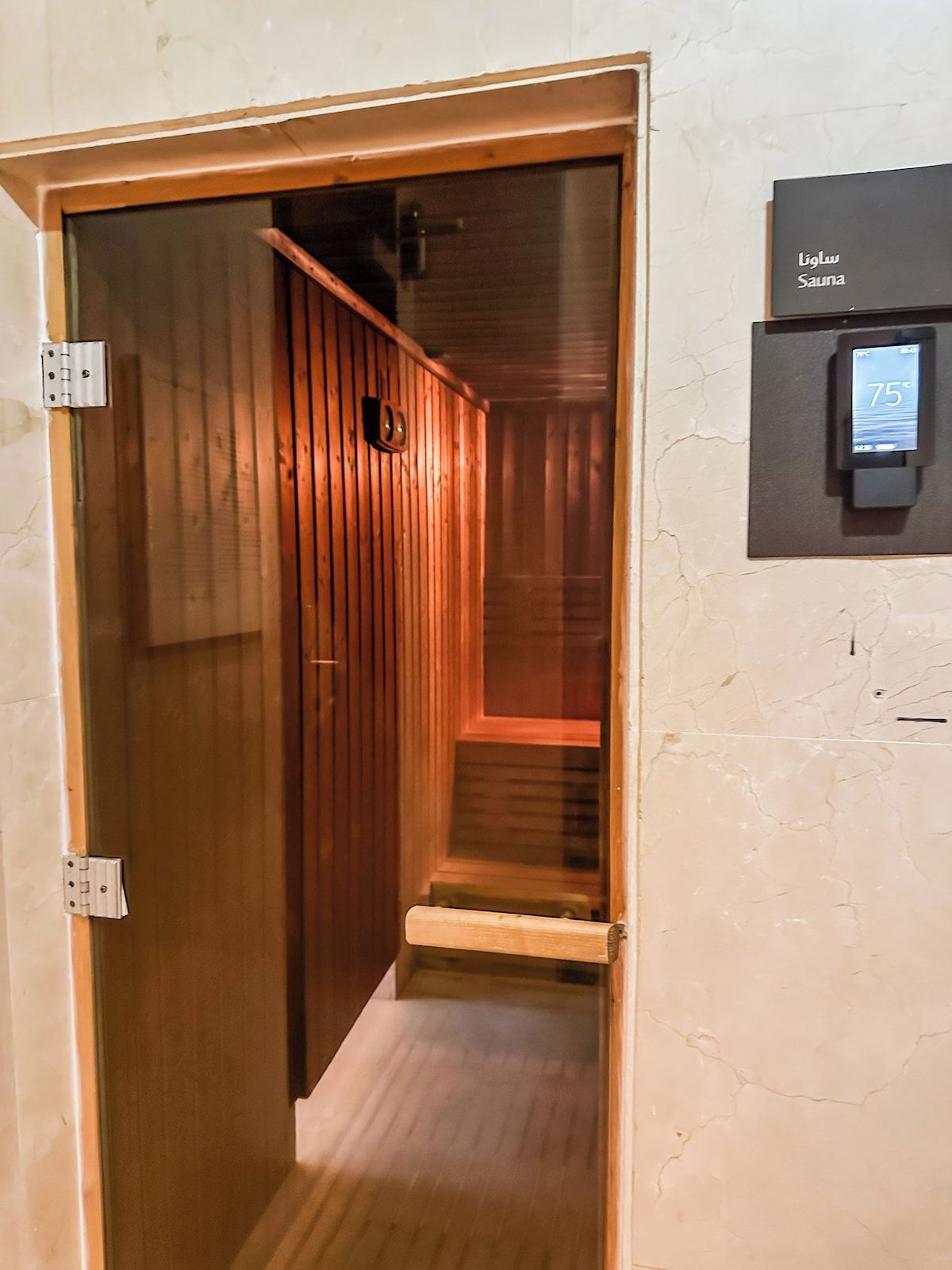 A sauna room with wooden walls and a digital thermostat displaying 75 degrees.