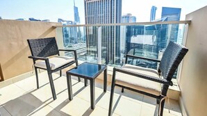 Un balcon agrémenté de fauteuils en osier et d’une petite table, offrant une vue sur un paysage urbain dominé par des bâtiments modernes.