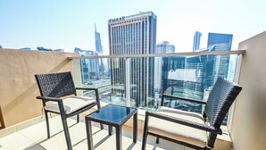 Een balkon met twee rieten stoelen en een kleine tafel, met uitzicht op een stadsgezicht met moderne gebouwen.