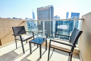 Varanda com duas cadeiras de vime e uma pequena mesa, com vista para um horizonte urbano repleto de edifícios modernos.