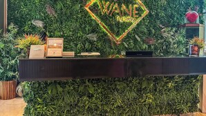 Een receptiebalie met een groene wand als achtergrond, een neonbord waarop 'WANE' staat en een kleine plant in een pot aan de rechterkant.
