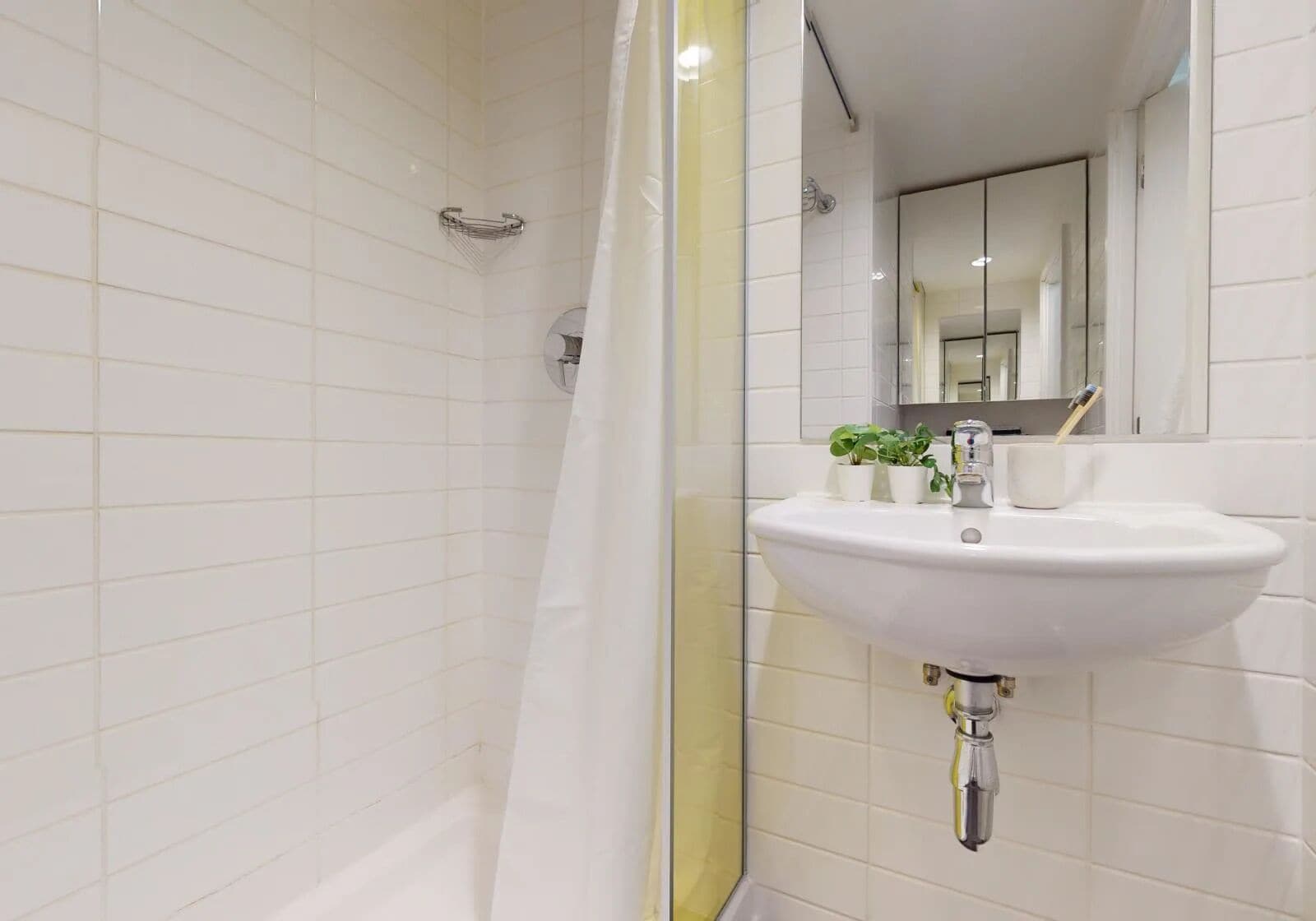 A bathroom with white tiled walls, a white sink with a mirror above it, and a shower curtain.