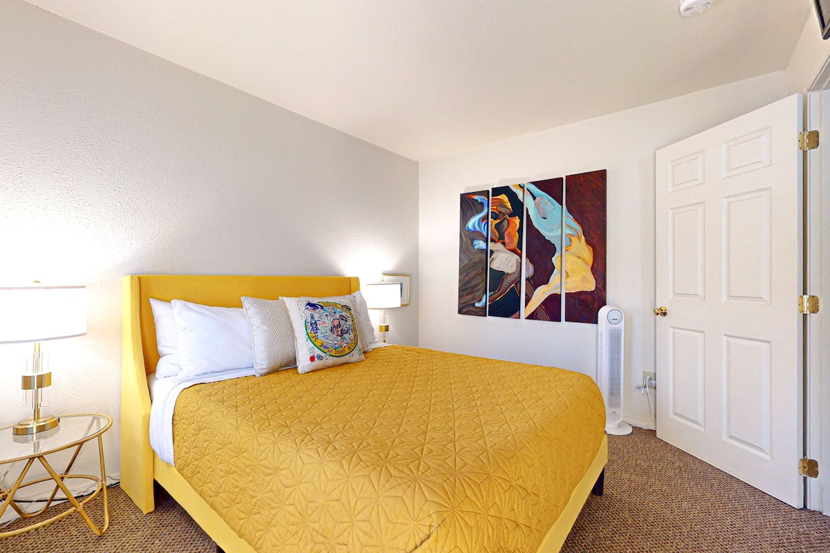 A hotel room with a large bed, a bedside table with a lamp, a wall-mounted artwork, and a door.