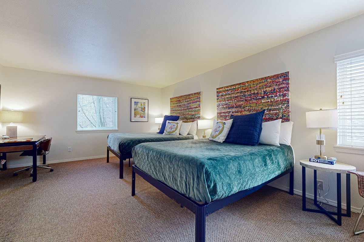 A hotel room with two beds, a desk, and a window.
