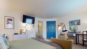 A hotel room with a bed, a desk, a chair, a TV, and a door. - The Washington Hotel (Port Townsend)