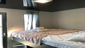 Un dormitorio con cama, ventana con cortinas, puerta y una lámpara en el techo.