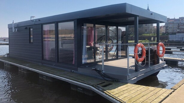 Una estructura flotante moderna con amplios ventanales, terraza cubierta y boyas salvavidas.