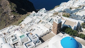 A coastal town with white buildings and a prominent blue-domed structure. - Ocean Caldera View Villa by Dalmyra Estate (Santorini)