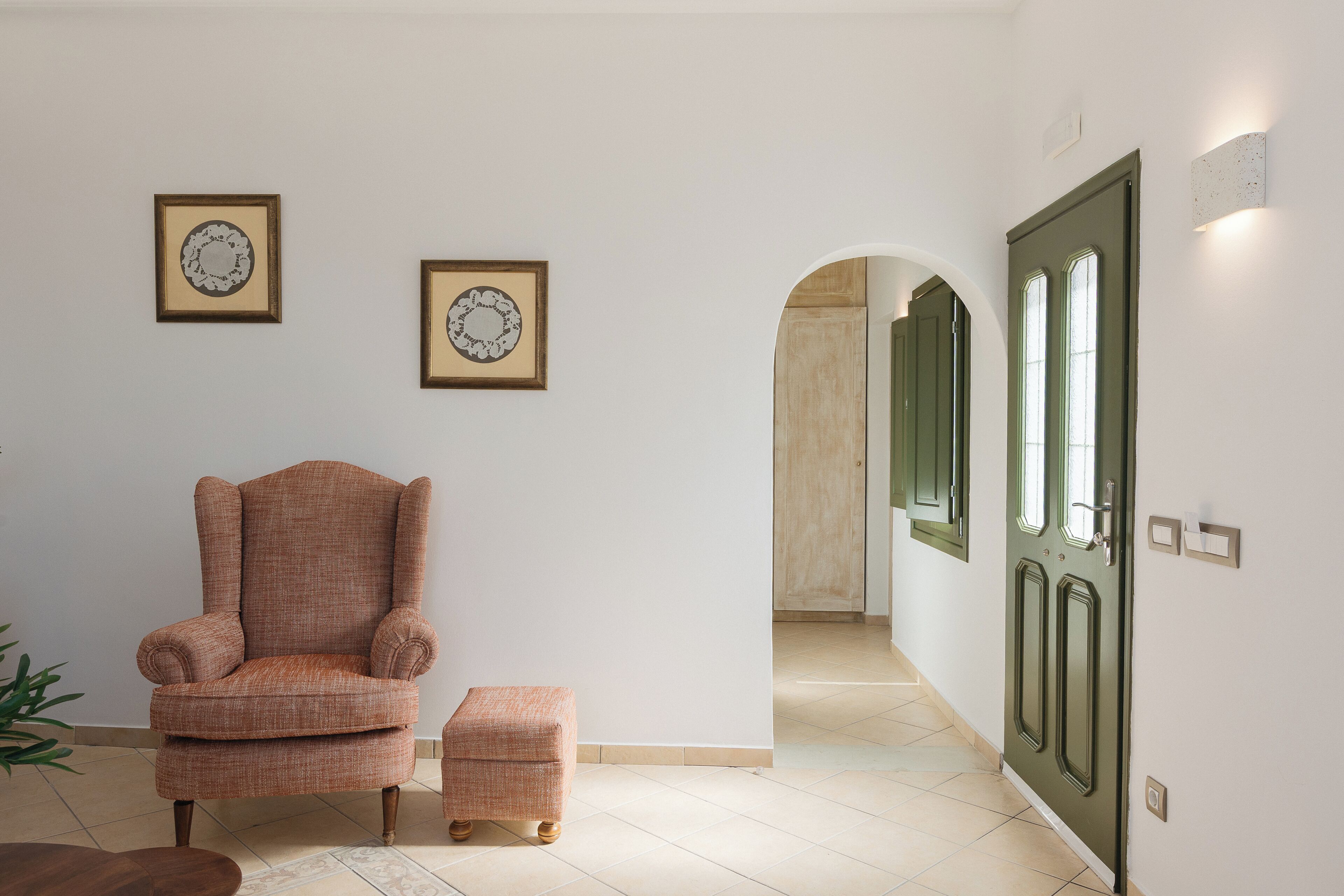 Um quarto com uma poltrona grande, um banquinho pequeno e duas decorações emolduradas na parede.