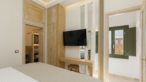 A bedroom with a bed, a TV mounted on a wooden shelf, a small stool, and a door leading to a balcony. - Ocean Caldera View Villa by Dalmyra Estate (Santorini)