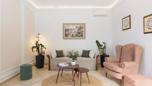 A living room with a sofa, a coffee table, a pink armchair, and two potted plants. - Ocean Caldera View Villa by Dalmyra Estate (Santorini)