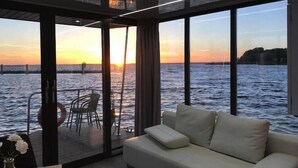 Un interior moderno con sofá y mesa, amplias ventanas con vista al mar y al atardecer.