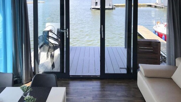 Una habitación con un amplio ventanal corredero que da a una terraza de madera con vistas al agua.