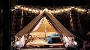 A tented accommodation with a stone wall backdrop, string lights, and a bed with pillows.