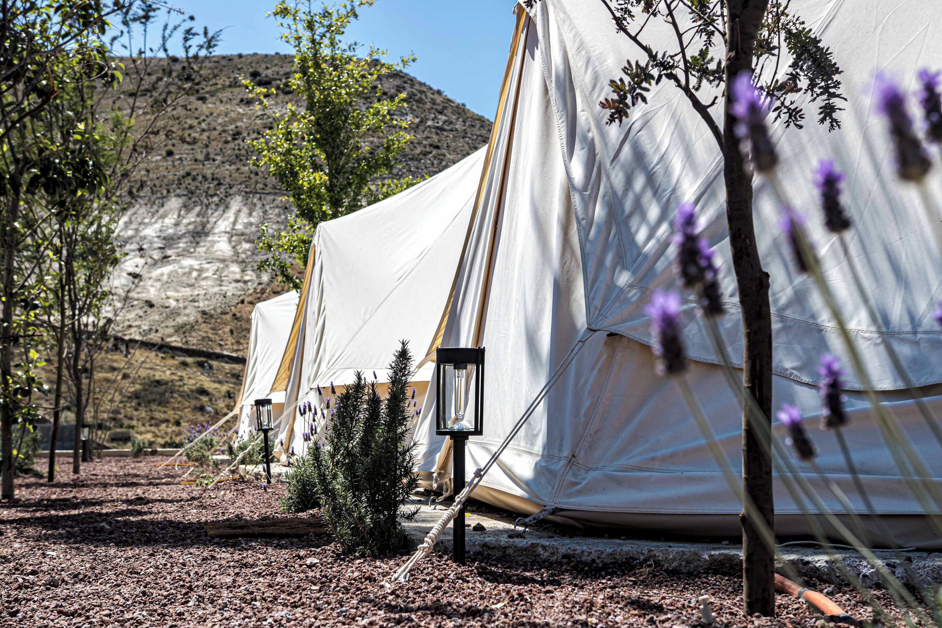Un campamento con tiendas de campaña, un farol y una ladera rocosa al fondo.