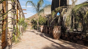 A stone pathway leading through a rustic building with wooden beams and stone walls, surrounded by palm trees.
