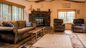 Una sala de estar acogedora con chimenea de piedra, sofá de cuero y dos sillones.