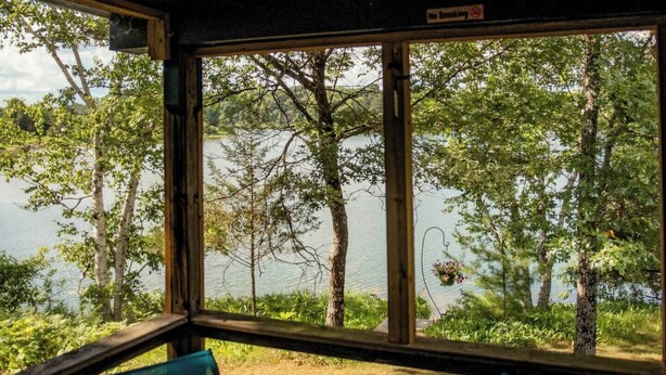 Una habitación con un ventanal grande con vistas a un lago, una cesta de flores colgante y dos sillas.