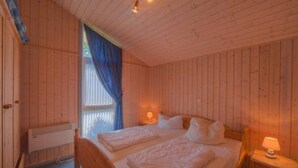 Habitación de cabaña de madera con dos camas, una ventana con cortinas azules y un calentador en la pared.