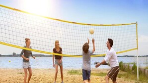 A group of people playing beach volleyball on a sandy court with a net, a body of water, and a clear sky in the background. - Skandinavisches Ferienhaus in Rechlin (Rechlin)