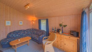 Interior acogedor de una cabaña con un sofá, un escritorio de madera, una silla y una mesita.