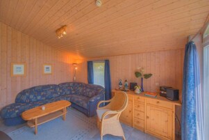 Interior acogedor de una cabaña con un sofá, un escritorio de madera, una silla y una mesita.