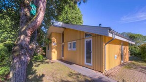 Un bâtiment jaune, de plain-pied, avec un petit porche et une porte.