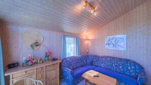 L’intérieur d’un chalet accueillant, avec un plafond en bois, un canapé, une table en bois, une chaise, un bureau avec une lampe et une fenêtre.