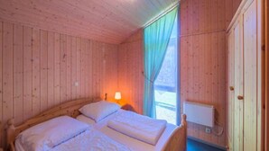 Une chambre dans un chalet en bois, avec deux lits, une table de chevet, une lampe et une fenêtre avec des rideaux.
