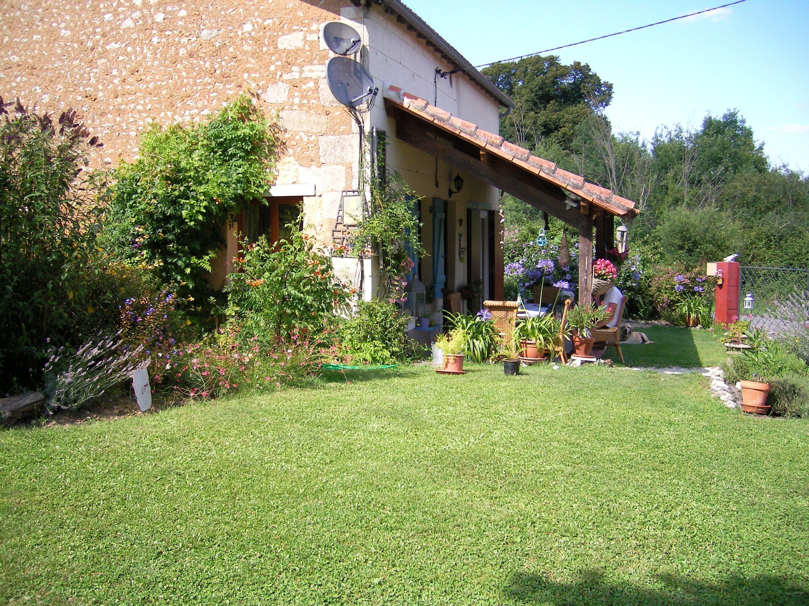 A rustic stone house with a covered porch, surrounded by a well-maintained garden with various potted plants and flowers.