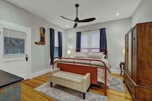 A bedroom with a bed, a bench, a wardrobe, a ceiling fan, and a window with curtains.