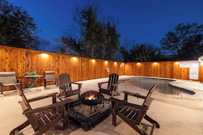 A wooden deck with a fire pit, outdoor seating, and a pool.