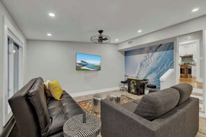 A modern living room with a sofa, ottoman, and a painting of a landscape.