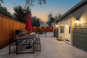 A patio with a table and chairs, a barbecue grill, and a wooden fence.