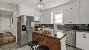 Una cocina con armarios blancos, un refrigerador de acero inoxidable, una isla de madera y un taburete de bar.