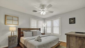 Un dormitorio con una cama, ventilador de techo, mesita de noche, lámpara y cómoda.