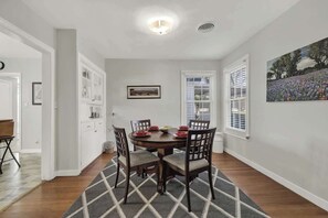 A dining area with a round table, chairs, a rug, and a painting on the wall. - Leicht Haus Hot-Tub & FirePit 5 blks to Main St! (Fredericksburg)