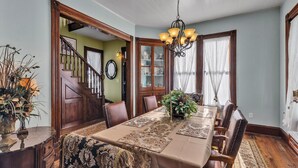 Un comedor con una mesa larga, sillas de madera, una araña y una escalera que lleva a otra habitación.