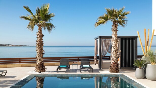 A poolside area with two lounge chairs, a small table, and a seating area with a view of the sea. - Infinity Blue and Golden Sky (Vir)