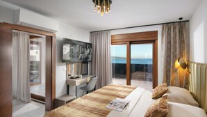 A modern hotel room with a large bed, a desk, a chair, and a view of the sea. - Infinity Blue and Golden Sky (Vir)