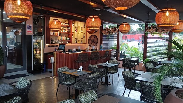 A restaurant with wicker furniture, a bar area, and large hanging lights. - Grey Courts (Accra)