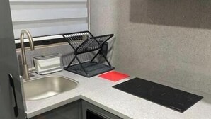 A compact kitchen with a sink, a black tray, a red mat, and a built-in oven. - Grey Courts (Accra)